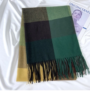 Close-up of green and yellow checkered scarf with long tassels on white fabric