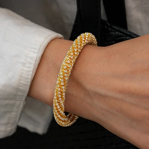 Gros plan d'un bracelet manchette doré serti de strass porté sur le poignet féminin