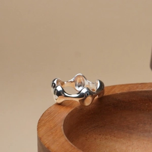Artistic close-up of a silver irregular wave textured ring on a brown wooden bowl edge