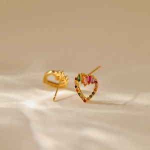 Macro shot of gold hollow heart earrings with colorful zircon stones on beige fabric