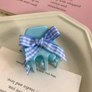 Detail of light blue hair claw clip with floral bow placed on a ceramic tray