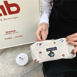 Close-up of beige canvas pencil case featuring cat embroidery and brand logo patch