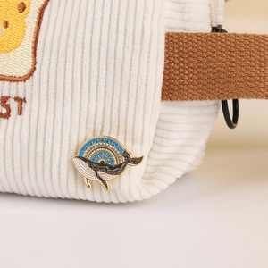 Minimalist whale enamel pin with blue and gold waves on white corduroy bag with strap