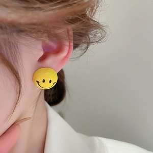 Close-up of a model wearing the yellow cartoon smiley face stud earrings on her ear
