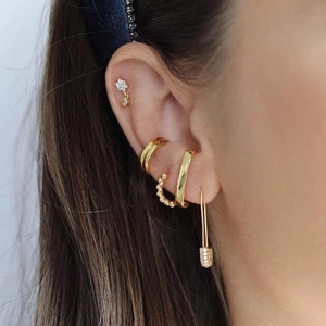 Stack of gold paperclip earrings and crystal ear cuffs on model ear for a layered jewelry look