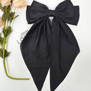 Detail view of large black satin bow hair clip with elegant long ribbon tassels on white