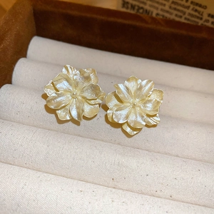 Macro detail of creamy camellia flower earrings with layered petals on velvet