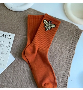 Close-up of orange ribbed knit mid-calf socks with detailed bee embroidery patch