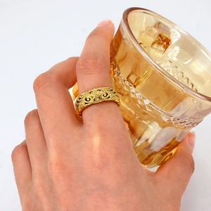 Minimalist gold-plated hollow pattern wide band ring worn by a model holding a glass cup