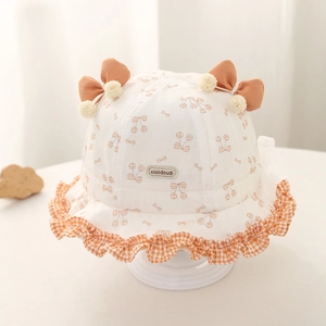 Détail du chapeau bébé avec imprimé cerise, nœud orange et bord volanté à carreaux