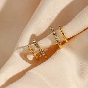 Macro view of gold double layered ear cuff with white zircon stones on satin fabric