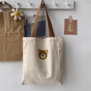 Detail view of cream canvas tote bag featuring a cute brown cartoon bear and straps