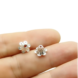Close-up of small silver flower bead caps for DIY jewelry making held by fingers