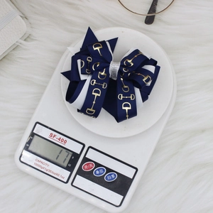 Navy blue and white equestrian bow hair clip with gold horsebit pattern on a scale