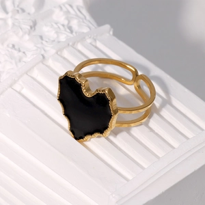 Detail of adjustable gold ring with black enamel heart inlay on a white relief column