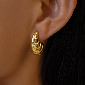 Gros plan d'une boucle d'oreille dorée en forme de coquillage à texture nervurée