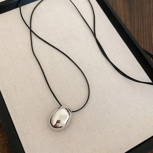 Close-up of polished silver oval pendant on black cord necklace in linen jewelry tray