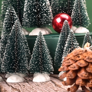 Mini green snowy Christmas trees set with ornaments and pine cone on wooden table