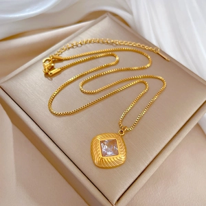 Detail of a square zircon pendant on a gold box chain necklace over silk fabric