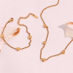 Detail view of 18K gold-plated stainless steel heart necklace and bracelet on wet pink background