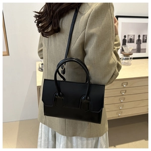Black PU leather tote bag with top handles and shoulder strap shown in a modern home