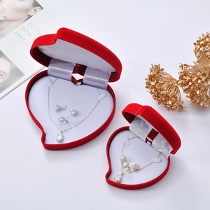 Red heart-shaped flocked jewelry box with gold and silver jewelry sets on a white background