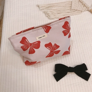 Detail of canvas makeup bag featuring red bow patterns and top zipper closure
