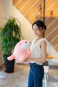 Detailed view of pink sea otter plush being held by hands in a warm indoor setting