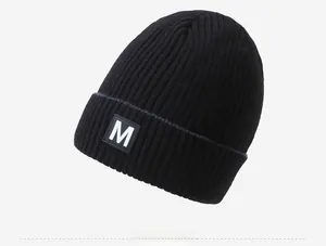 Detail view of the black ribbed knit beanie featuring a white letter M logo patch