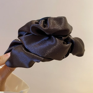 Detail of a dark brown pleated satin scrunchie showing glossy texture and rich folds