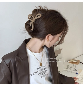 Detail view of large matte coffee bow hair claw clip styled on a model in a cozy setting