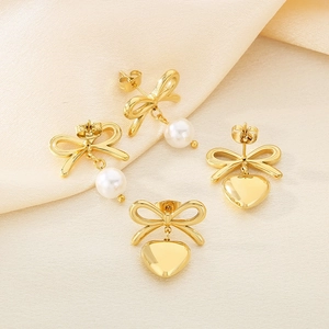 Elegant gold bow earrings set with white pearls and heart pendants on beige silk