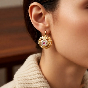 Close-up of a vintage gold hollow earring with a red gemstone and clear accents on a model