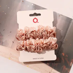 Close-up of pleated satin scrunchies in peach pink and champagne gold on display card