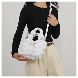 Close-up of a white quilted puff handbag featuring heart patterns and a gold bow detail