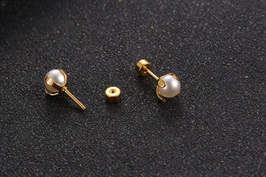Detail view of gold titanium steel stud earrings with white mini pearls on a black background