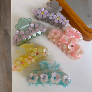 Macro shot of five pastel acetate flower hair claws in pink, green, yellow, and blue