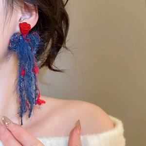 Dettaglio di nappe in peluche blu fatte a mano e fiori rossi su orecchini a lobo lunghi