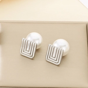 Macro view of square metal earrings with layered spiral textures and white round pearls