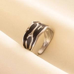 Close-up of silver ring with black drip oil texture on elegant pleated satin background
