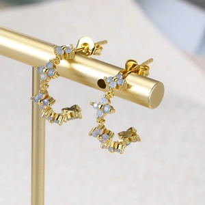 Macro shot of gold-plated floral C-shaped earrings with light blue petals on a display stand