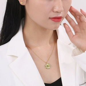 Detail of gold floral necklace and earrings set with green gemstones on model