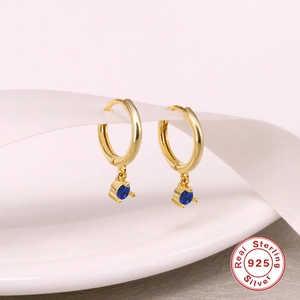 Macro shot of gold S925 silver hoop earrings with blue zircon drops and ribbon detail