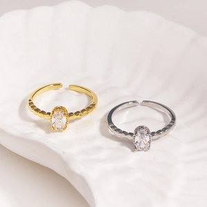 Detail of adjustable gold and silver rings with oval zircons on a white shell background