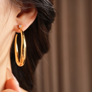 Close-up of a large golden C-shaped hoop earring with a small zircon stud on a model