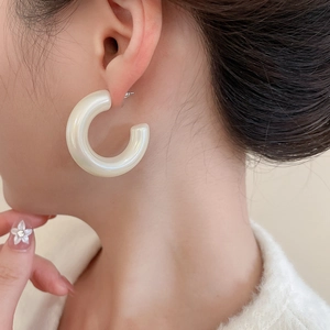Close-up of elegant cream-colored acrylic C-shape hoop earrings on a female model