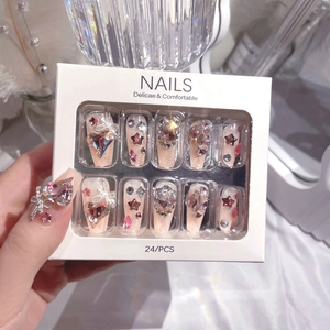 Detail of nude pink press-on nails with luxury rhinestones and bow in elegant packaging