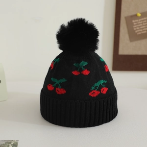 Detail of black winter knit hat featuring red cherry jacquard and soft faux fur pom-pom