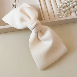 Close-up of a large cream-colored fabric bow hair clip with elegant pearl necklace detail