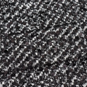 Close-up of black and white tweed fabric texture with shimmering sequins on the surface